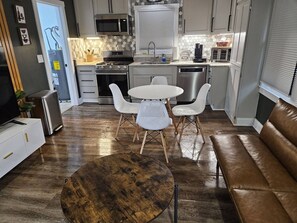 Una cucina moderna con mobili bianchi, un forno a microonde, un piano cottura e una lavastoviglie. Al centro, un tavolo rotondo in legno con sedie bianche.