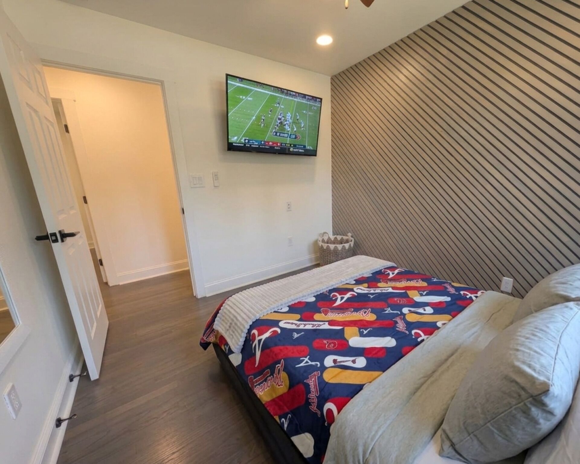 A bedroom with a bed, a television mounted on the wall, and a door leading to another room.