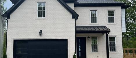 A two-story house with a garage, a front porch, and a small garden.