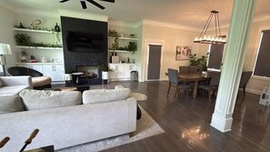 A modern living room with a sofa, a flat-screen TV, and a dining area with a table and chairs.