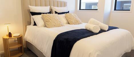 A neatly made bed with a headboard, a bedside table with a lamp, and a window with a view of the outside.