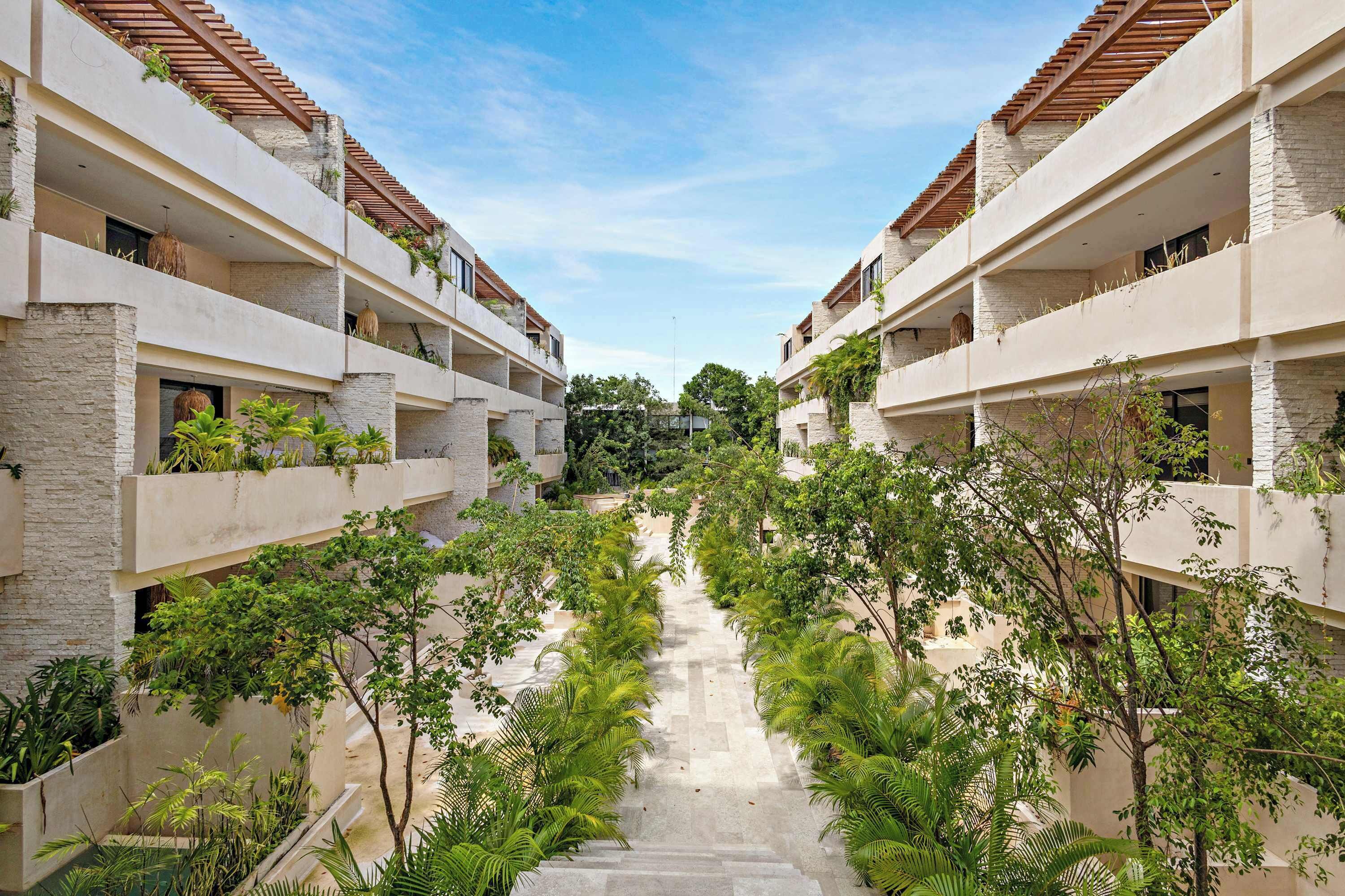 A multi-story hotel with a central courtyard surrounded by lush greenery and a clear sky.
