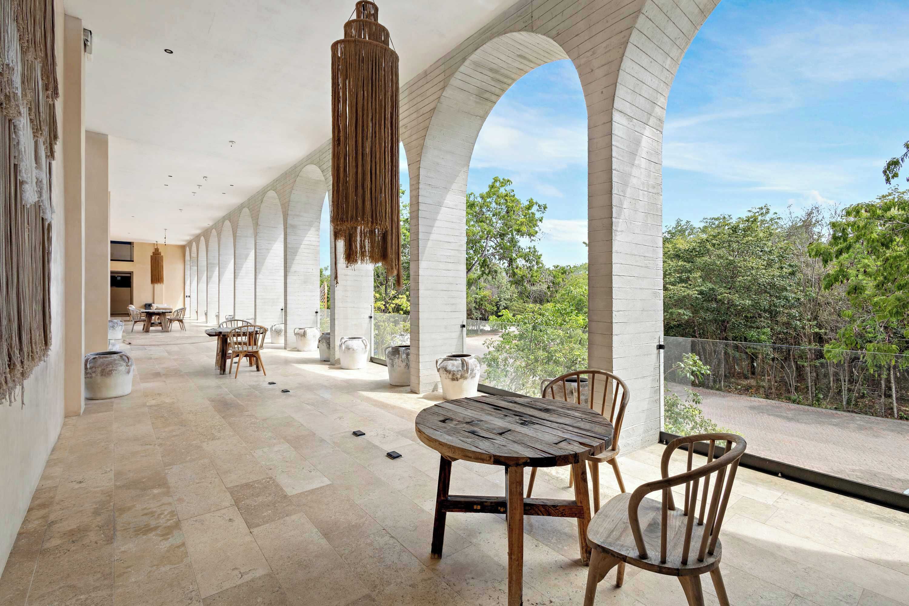 A spacious covered patio with a view of the surrounding greenery, featuring a rustic wooden table and chairs, and a hanging light fixture.