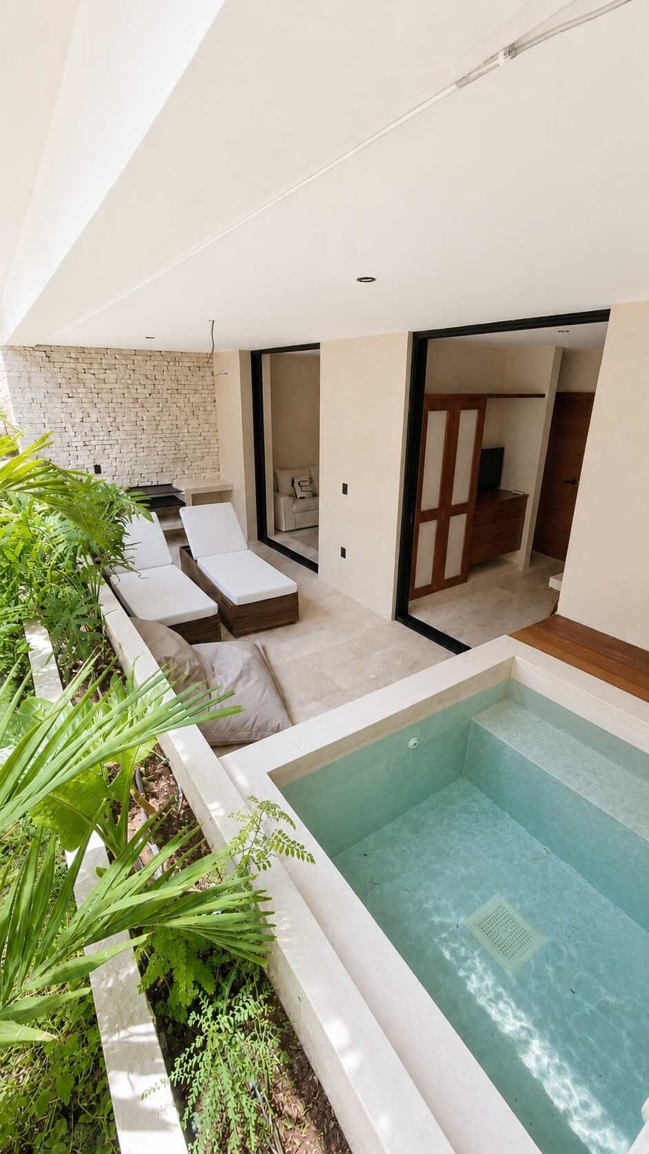 A modern outdoor pool area with lounge chairs, a stone wall, and a wooden deck.