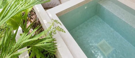 A modern outdoor pool area with lounge chairs, a stone wall, and a wooden deck.