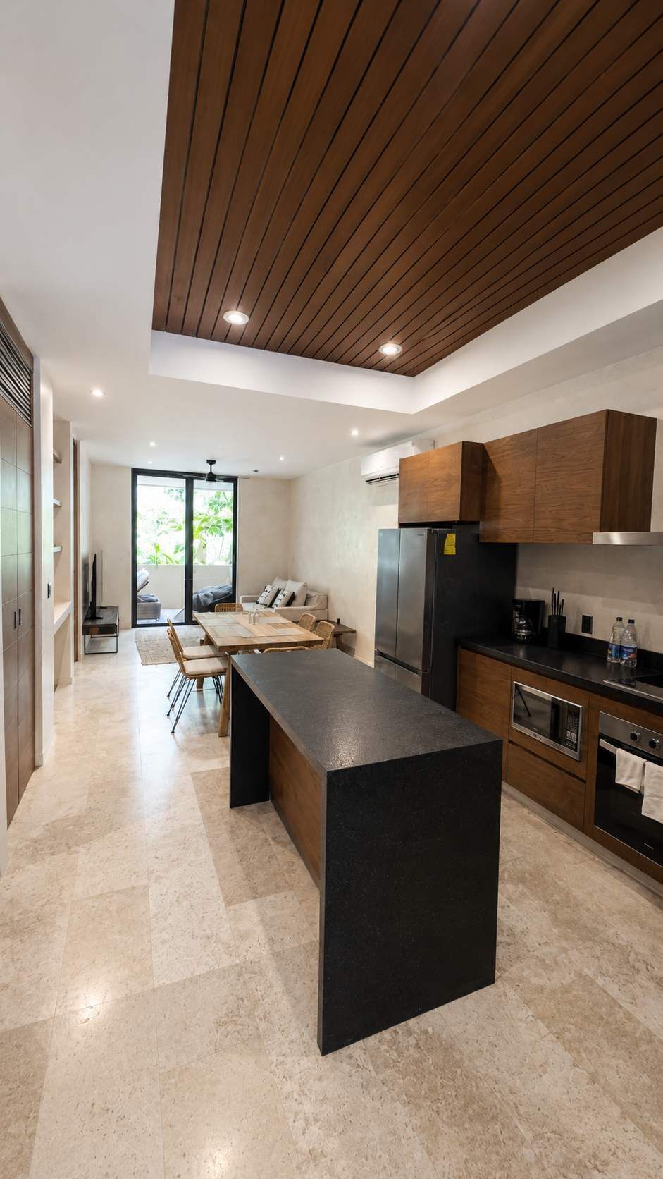 Une cuisine moderne dotée d’un îlot central, de meubles en bois et d’une grande fenêtre qui laisse entrer la lumière naturelle.
