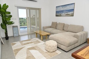 A living room with a sofa, a coffee table, a rug, a potted plant, and a painting on the wall. - Brand New Beach Villa with Pool, Walk to La Bougainvillea Restaurant and Bar (Governor's Harbour)