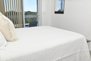 A bedroom with a bed, a window with blinds, and a view of greenery outside. - Brand New Beach Villa with Pool, Walk to La Bougainvillea Restaurant and Bar (Governor's Harbour)