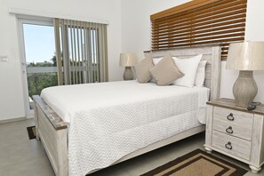 A bedroom with a bed, bedside tables, a lamp, and a view through the window. - Brand New Beach Villa with Pool, Walk to La Bougainvillea Restaurant and Bar (Governor's Harbour)