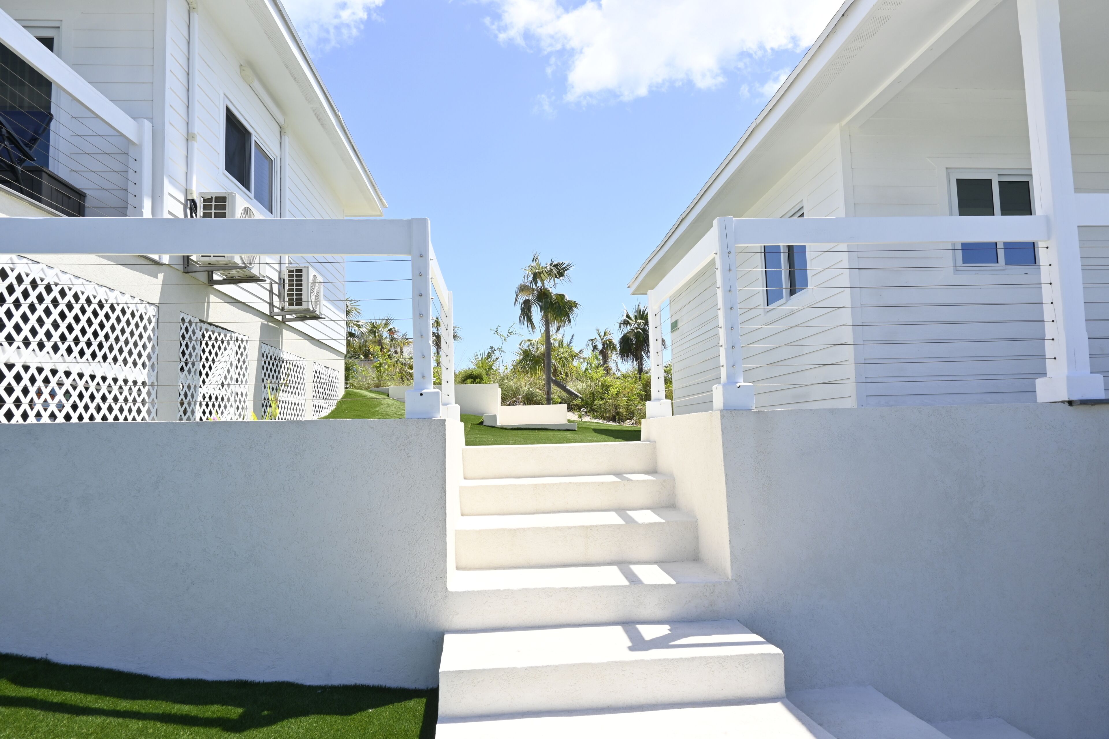 Ein modernes Gebäude mit weißer Fassade, einer Treppe aus Beton, die zu einem verschlossenen Eingang führt, und einem klaren Himmel im Hintergrund.