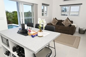 A modern living room with a dining area, a sofa, and a view of the outdoors. - Brand New Beach Cottage with Pool, Walk to La Bougainvillea Restaurant and Bar (Governor's Harbour)