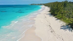 A beach with clear turquoise water, white sand, and dense green vegetation along the shoreline. - Brand New Beach Cottage with Pool, Walk to La Bougainvillea Restaurant and Bar (Governor's Harbour)