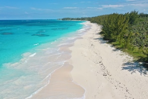 A beach with clear turquoise water, white sand, and dense green vegetation along the shoreline. - Brand New Beach Cottage with Pool, Walk to La Bougainvillea Restaurant and Bar (Governor's Harbour)