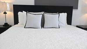 A bed with a white textured bedspread, two pillows with black trim, and a black headboard. - Brand New Beach Cottage with Pool, Walk to La Bougainvillea Restaurant and Bar (Governor's Harbour)
