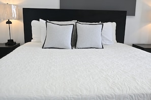 A bed with a white textured bedspread, two pillows with black trim, and a black headboard. - Brand New Beach Cottage with Pool, Walk to La Bougainvillea Restaurant and Bar (Governor's Harbour)