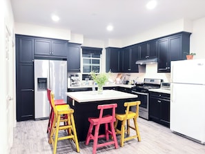 A modern kitchen with black cabinets, stainless steel appliances, and a central island with two chairs.