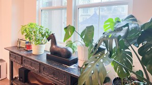 A room with a wooden desk, a potted plant, a decorative horse sculpture, and a window with blinds.