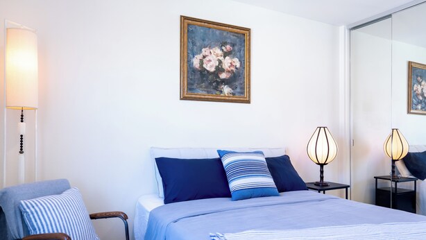 A hotel room with a bed, a chair, a lamp, and a painting on the wall.