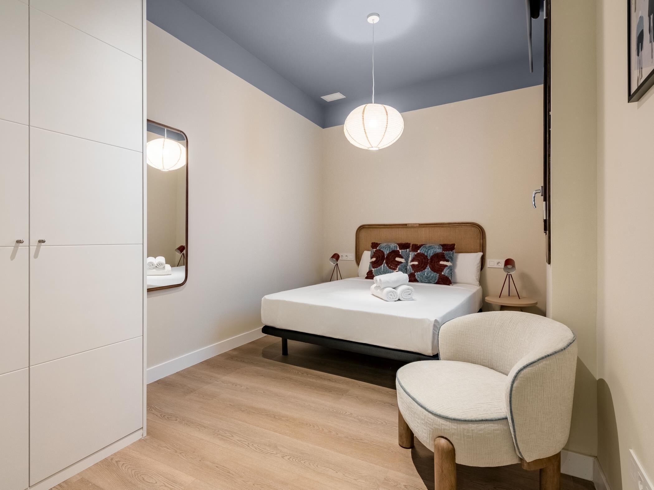 Une chambre à coucher comprenant un lit, une chaise, une armoire, un miroir et un luminaire suspendu.