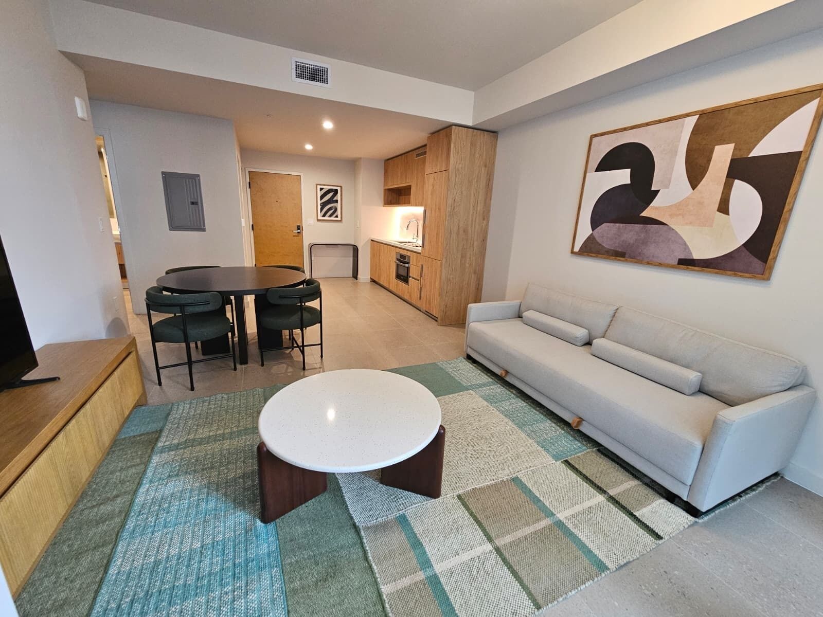 A modern living room with a sofa, a round coffee table, a dining table with chairs, and a kitchen area.