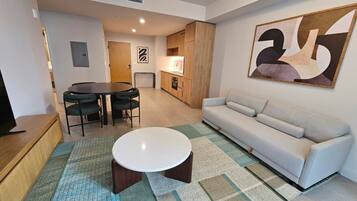 A modern living room with a sofa, a round coffee table, a dining table with chairs, and a kitchen area.