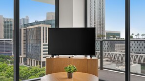 A modern hotel room with a large window, a flat-screen TV, a wooden table, and a potted plant. - The Crosby Miami Condos (Miami)