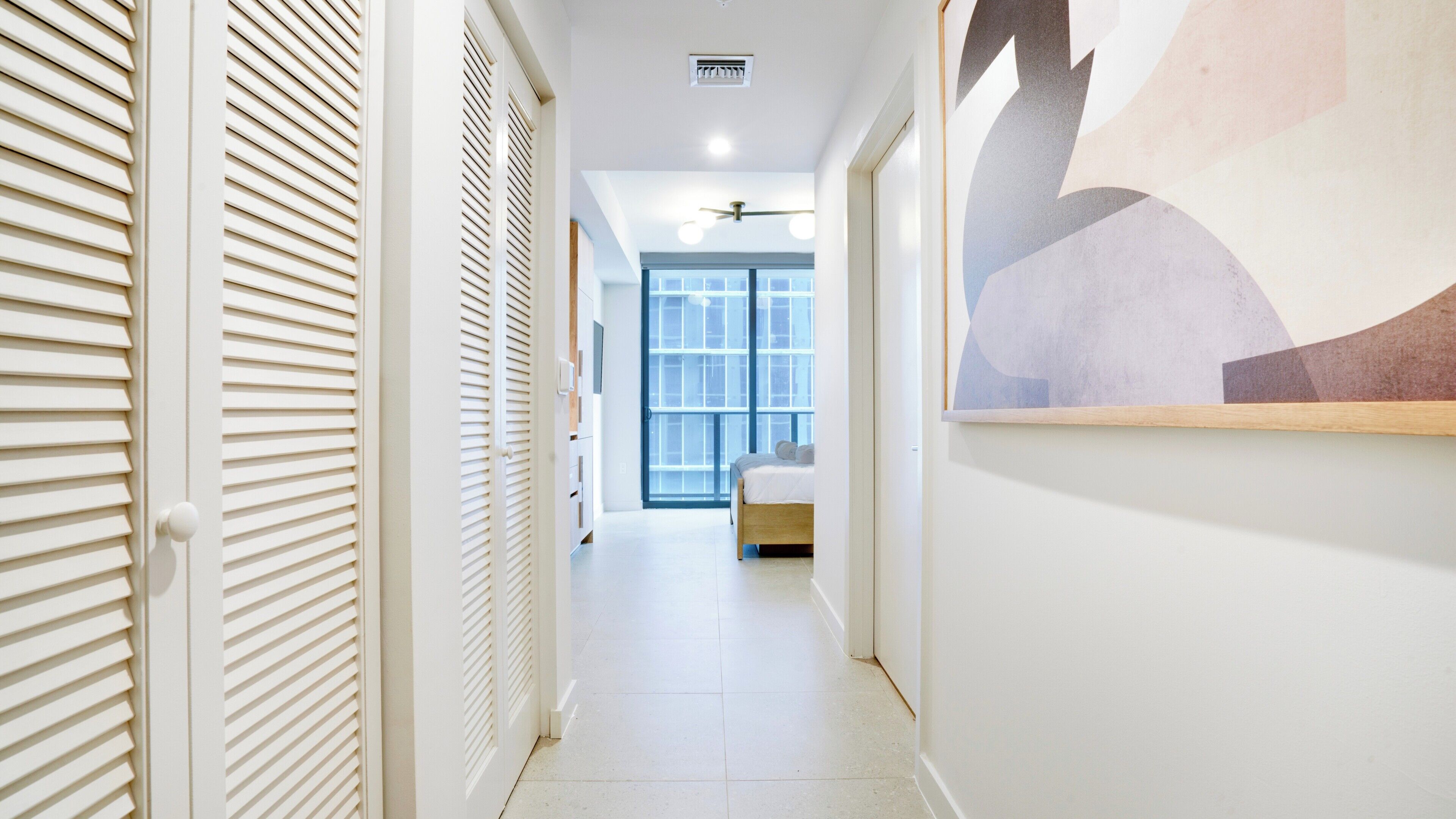 A hallway with a bed, a ceiling fan, and a large window.