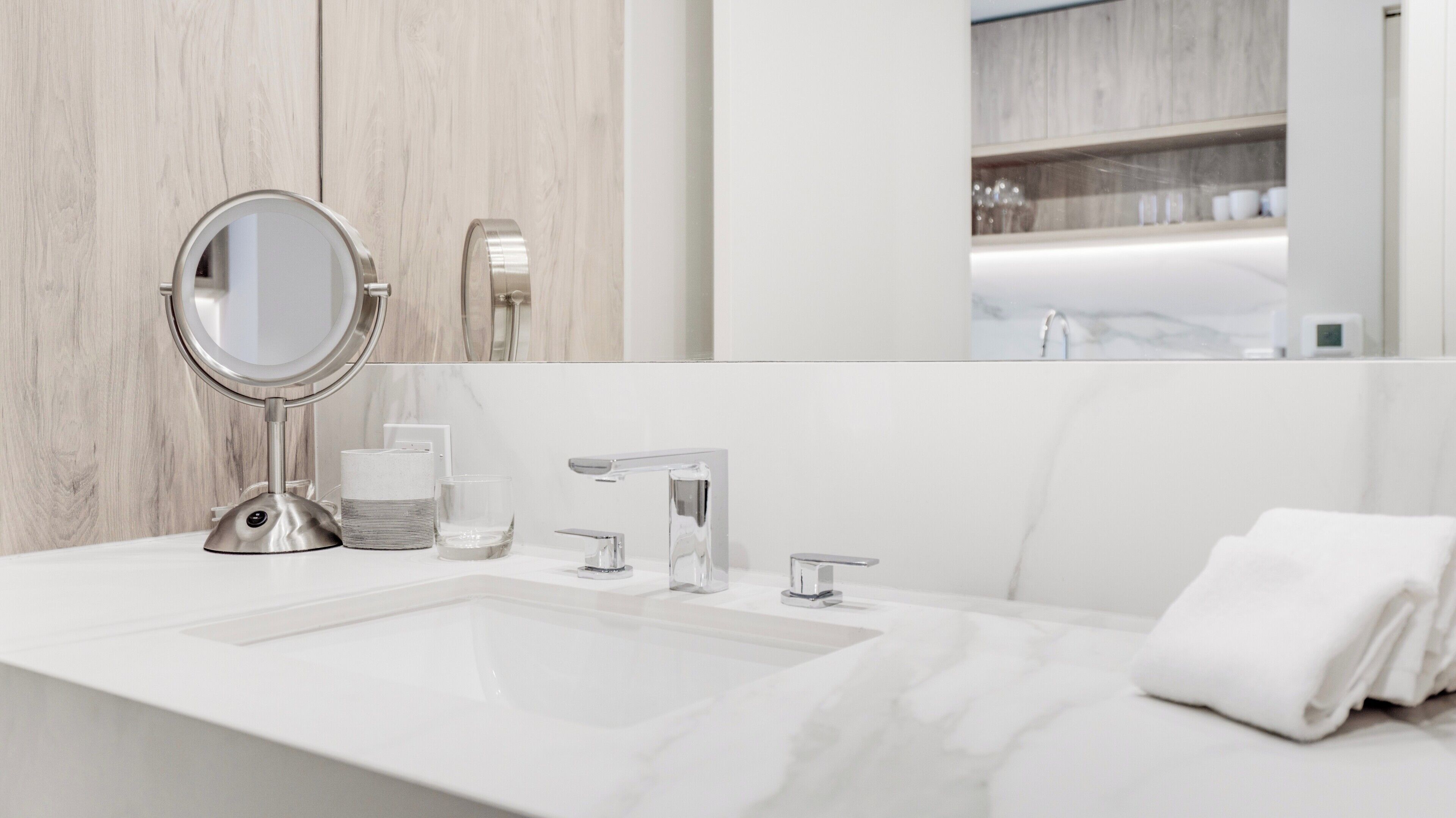 Un bagno moderno con un lavandino bianco, uno specchio rotondo, un rubinetto e un asciugamano.