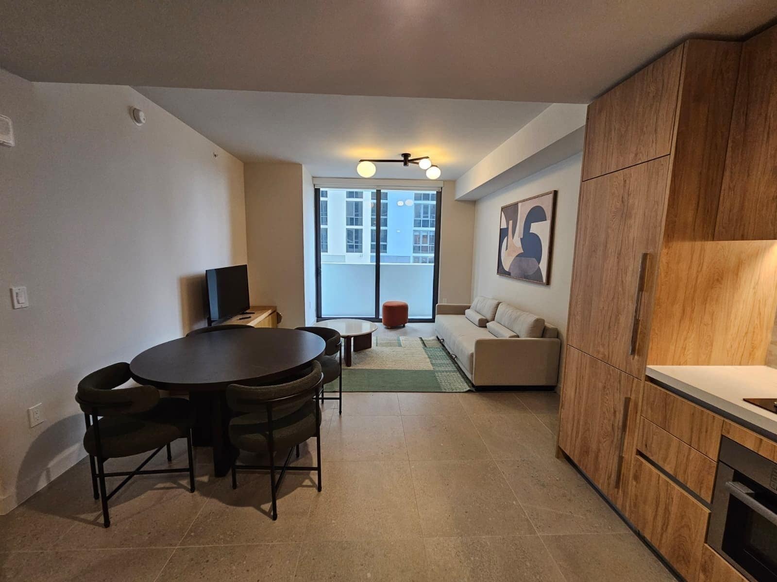 A modern apartment with a dining area, a sofa, a kitchen, and a large window.