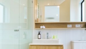 Ein modernes Badezimmer mit Duschkabine aus Glas, einem Holzkosmetikschrank mit Spiegel und einem weißen Waschbecken.