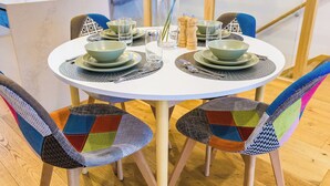 Ein runder Esstisch mit vier grünen Schüsseln und Tellern, silberbesteck und einem klaren Glas. Die Stühle sind farbenfroh mit Patchwork bezogen.
