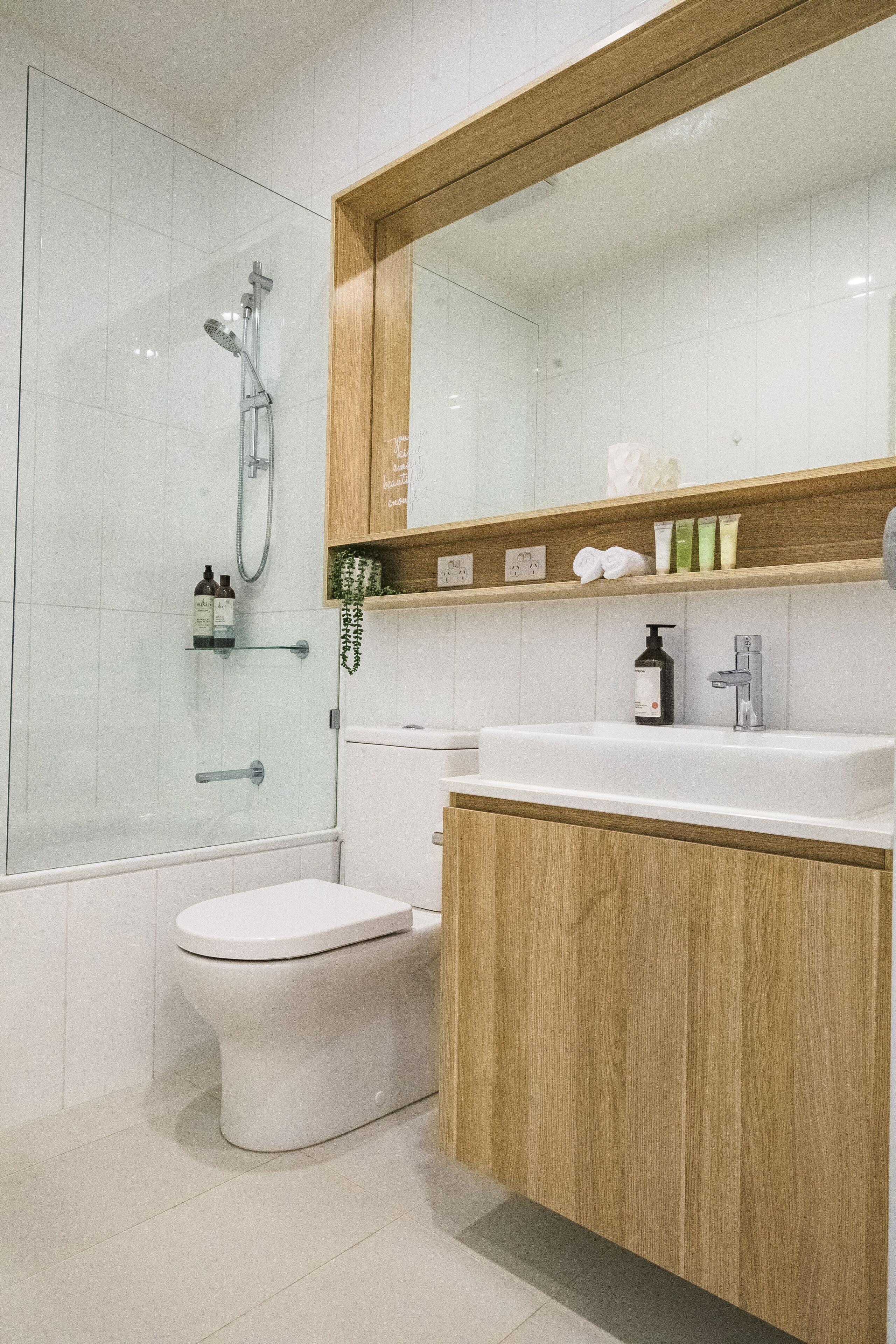 A modern bathroom with a glass shower enclosure, a toilet, a sink with a wooden vanity, and a mirror above the sink.
