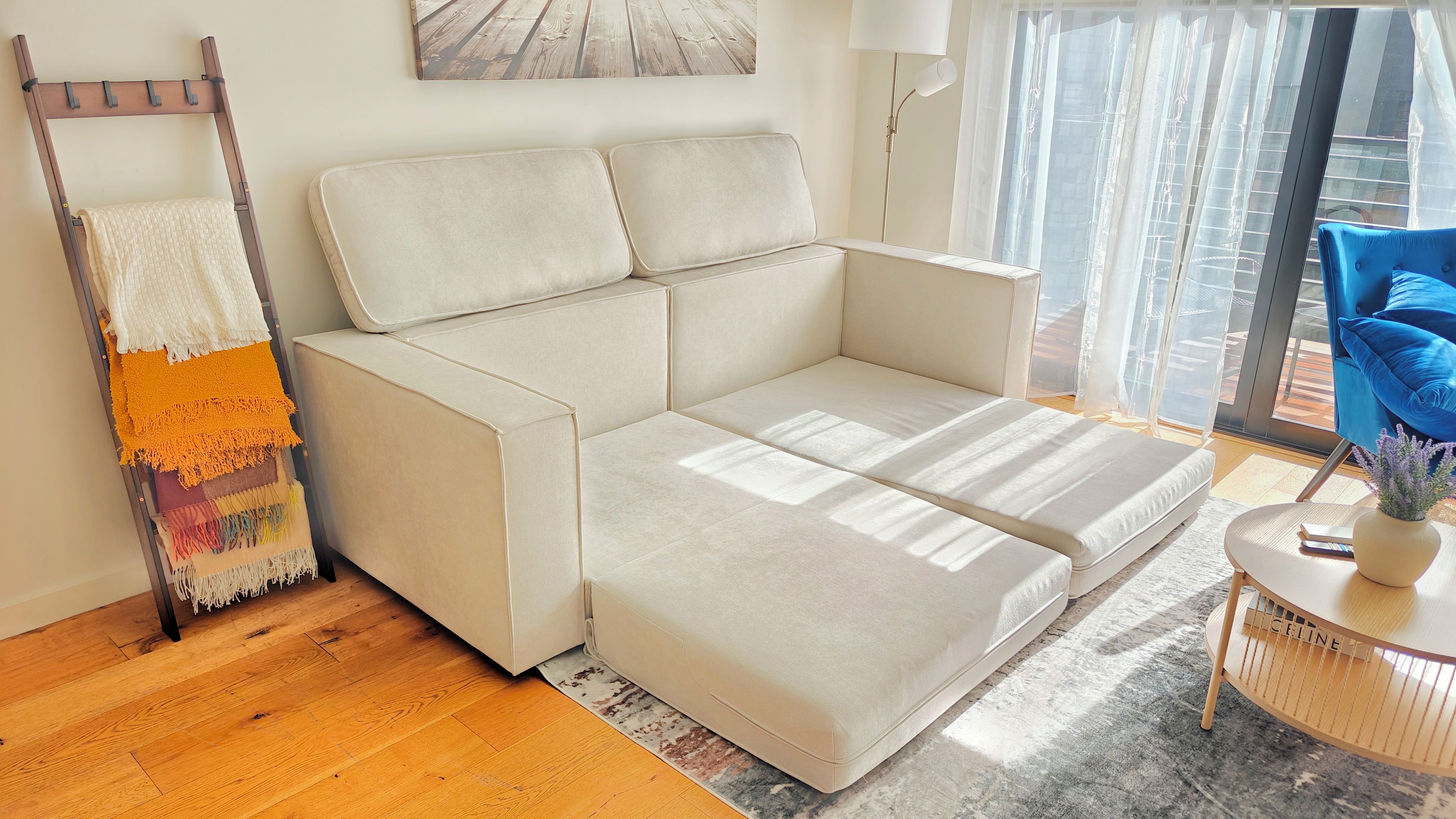 A modern living room with a sofa, a ladder, a rug, and a window with curtains.