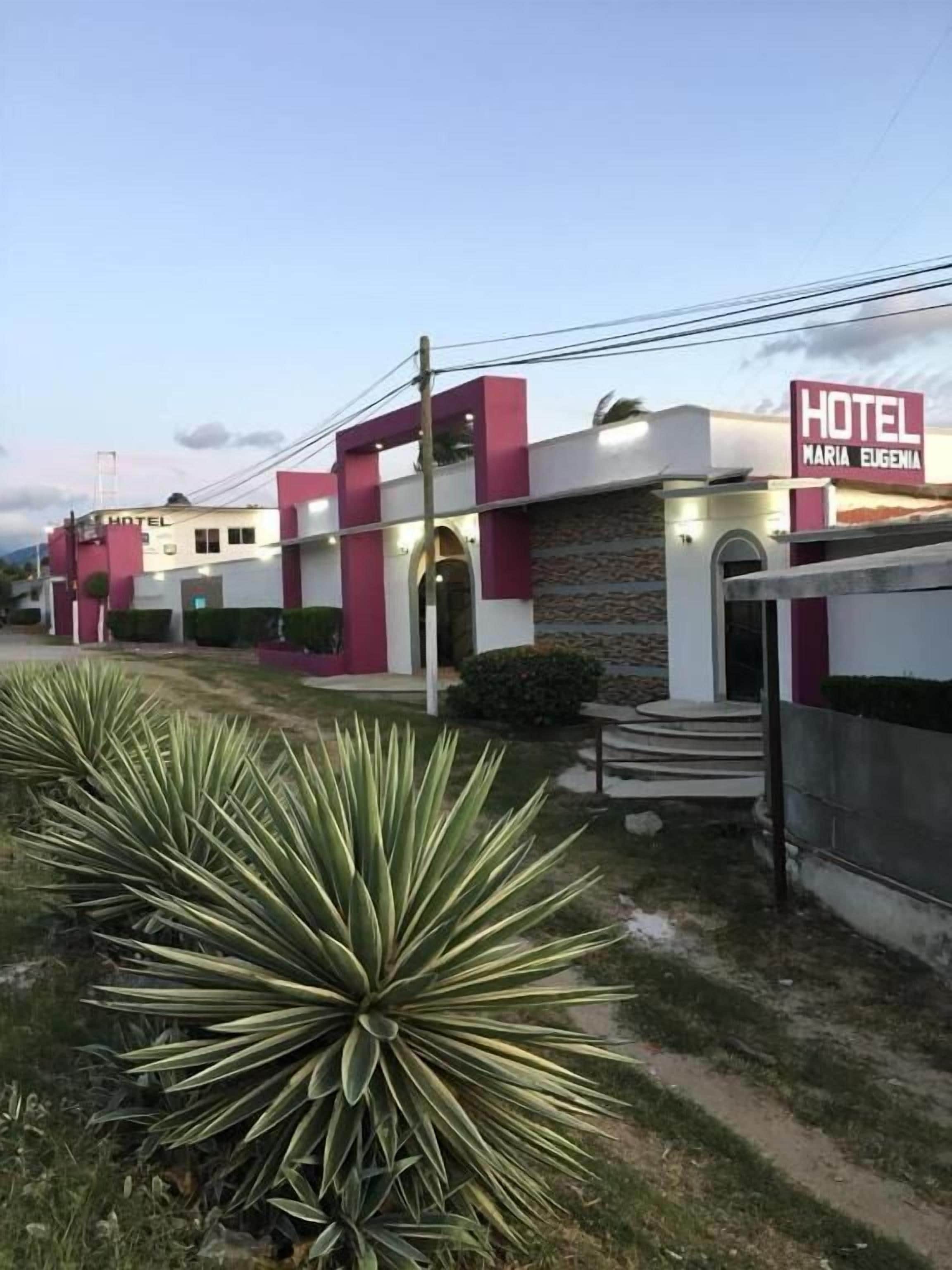 A hotel with a modern facade, a prominent sign, and a well-maintained lawn with agave plants.