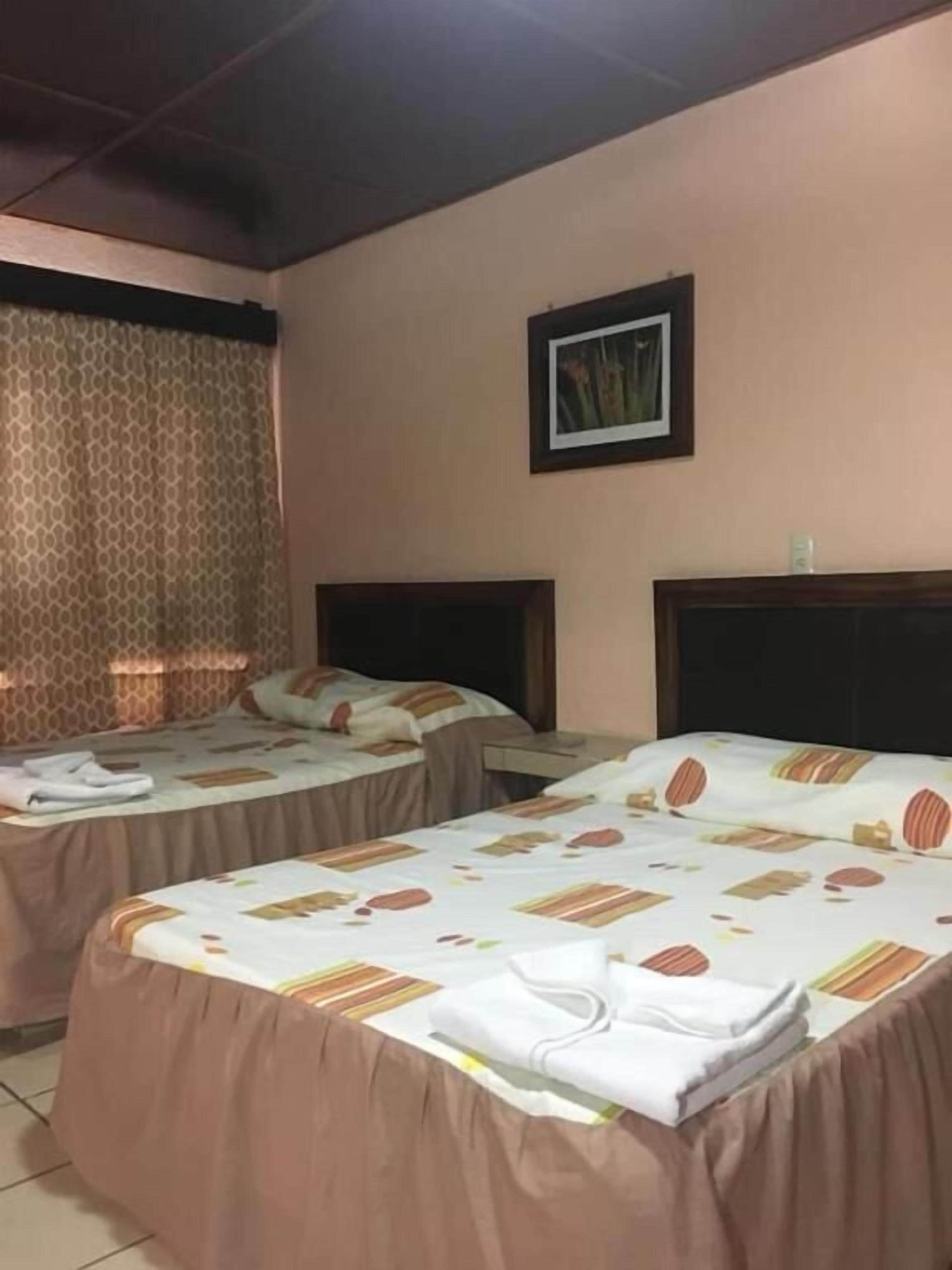 Quarto de hotel com duas camas, cabeceira, um quadro na parede e uma janela com cortinas.