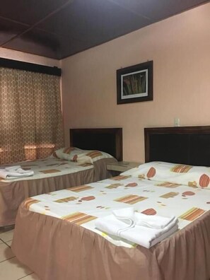 Habitación de hotel con dos camas, un cabecero, un cuadro en la pared y una ventana con cortinas.
