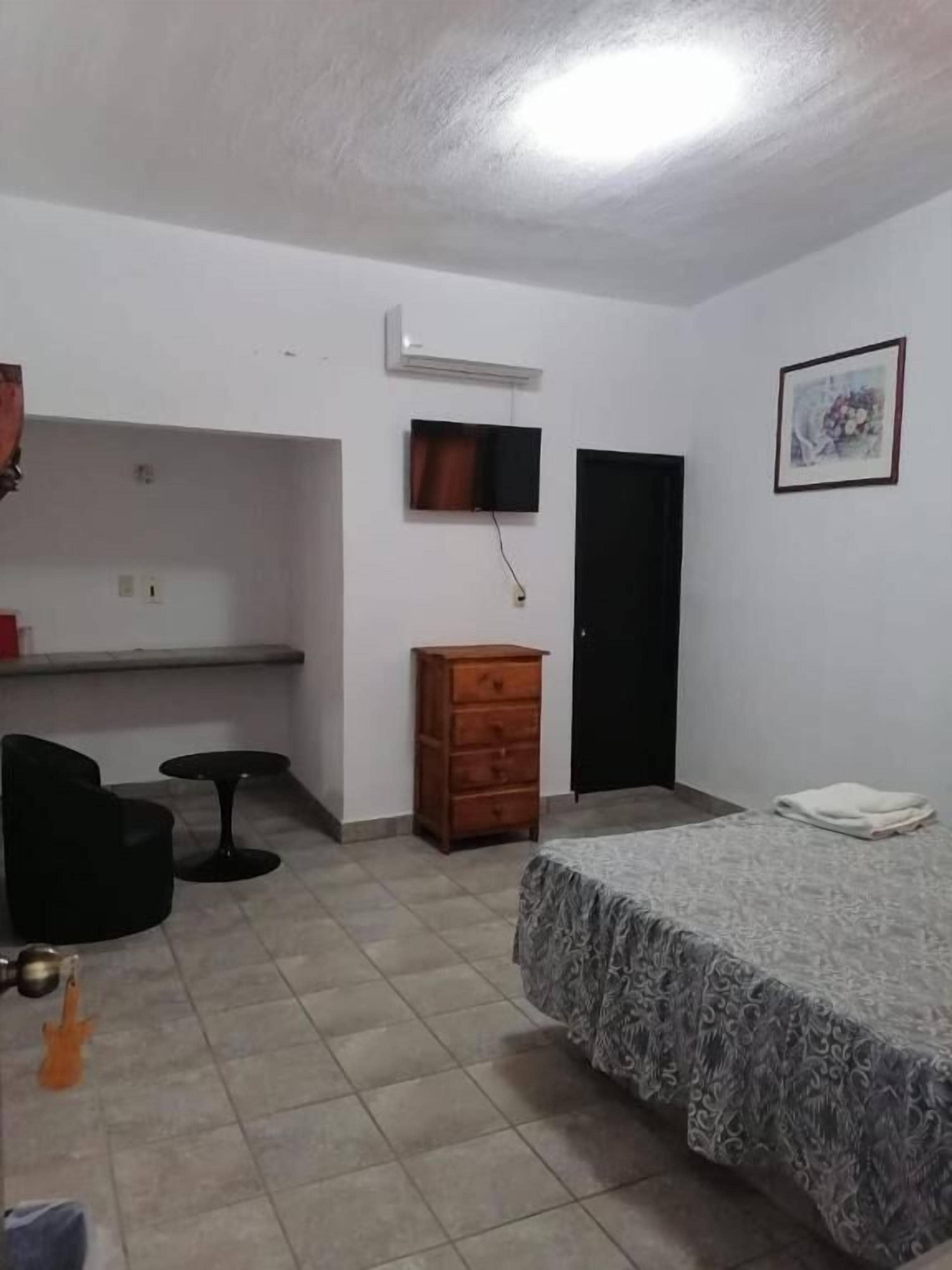 Quarto com cama, cômoda, escrivaninha, cadeira e televisão.