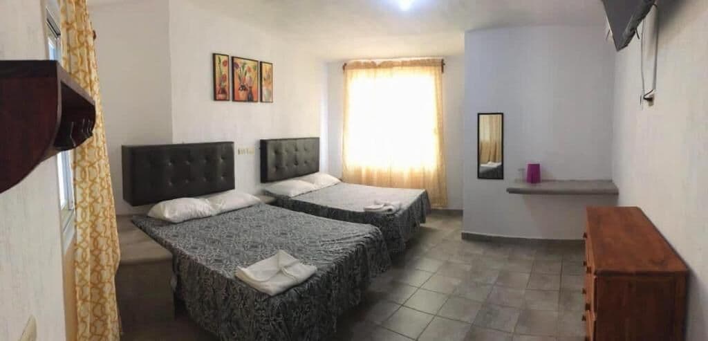 A hotel room with two beds, a small desk, a mirror, and a window with curtains.
