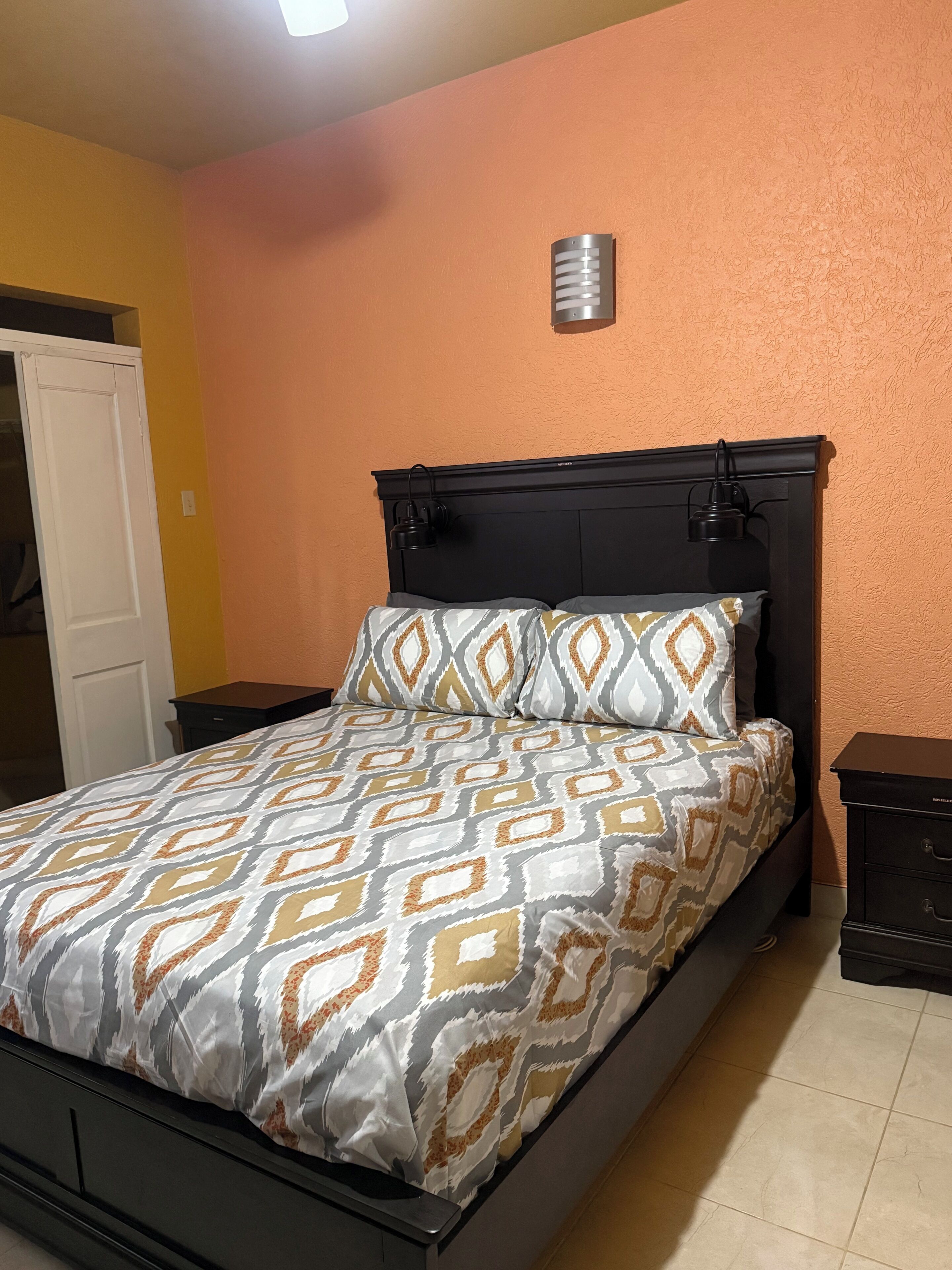 A bed with a patterned bedspread, a headboard, and a bedside table with a lamp.