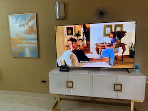 Un téléviseur posé sur un meuble blanc, avec une télécommande sur le dessus, cette dernière étant étiquetée « Télécommandes  ».