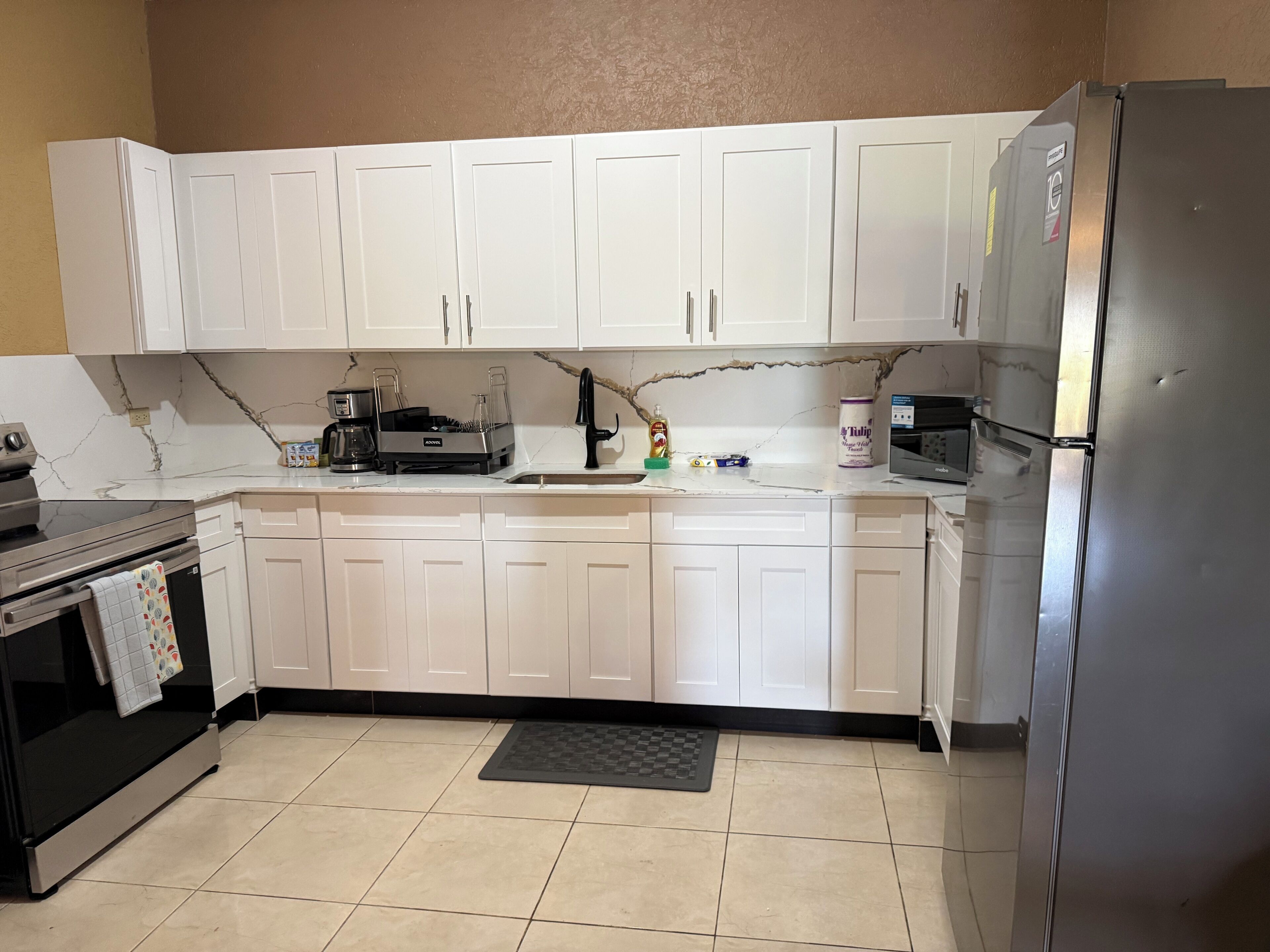 A kitchen with white cabinets, a black countertop, a stainless steel refrigerator, and a coffee maker.
