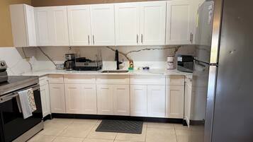 A kitchen with white cabinets, a black countertop, a stainless steel refrigerator, and a coffee maker.
