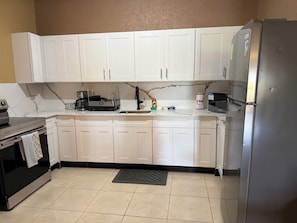 A kitchen with white cabinets, a black countertop, a stainless steel refrigerator, and a coffee maker. - 2BR Ironshore Stay with Pool & Gym • Near Airport, Beaches & Hip Strip (St. James Parish)