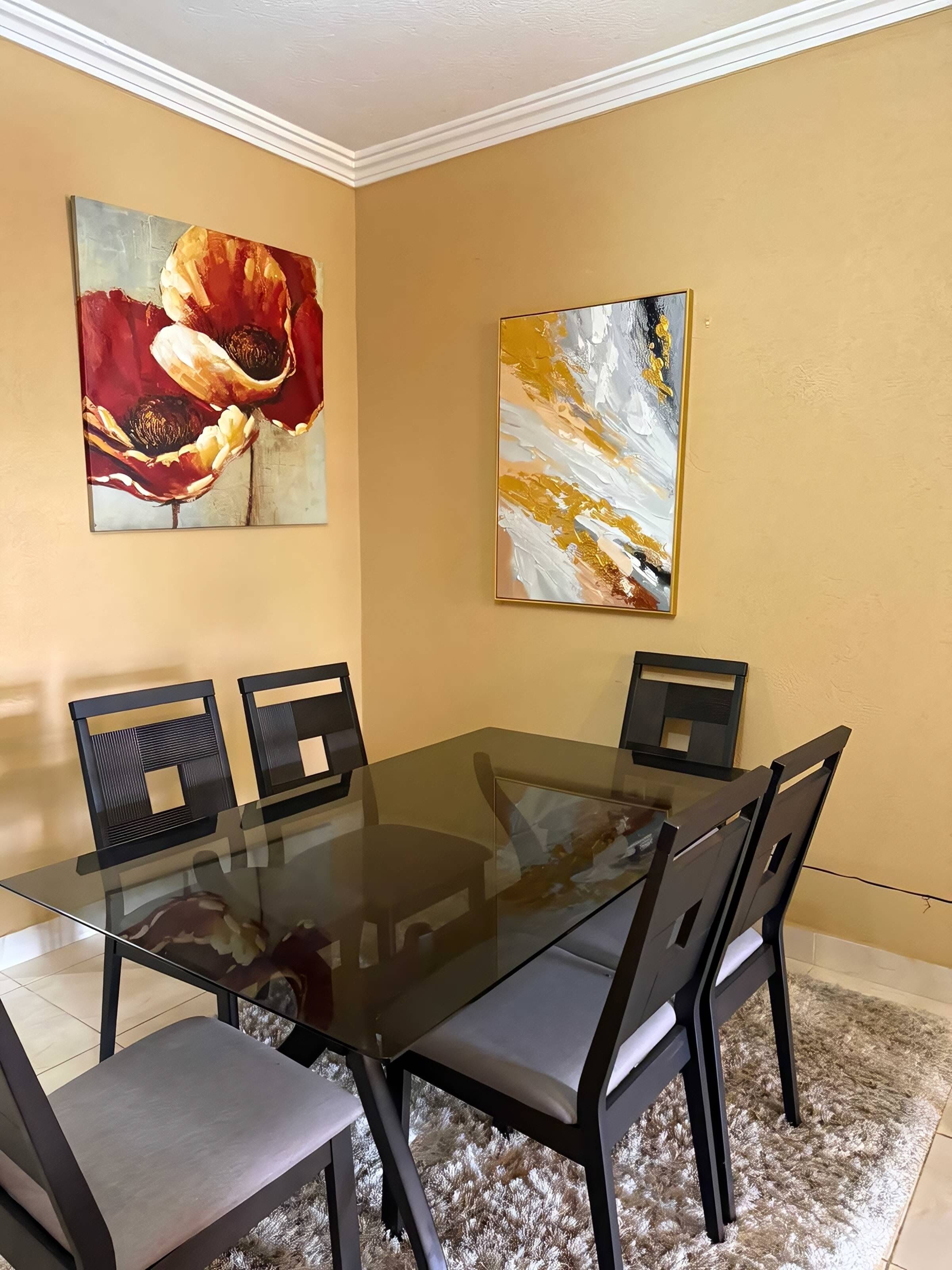 Une salle de conférence avec une table en verre et des chaises noires, deux tableaux accrochés aux murs et un tapis à motifs sur le sol.
