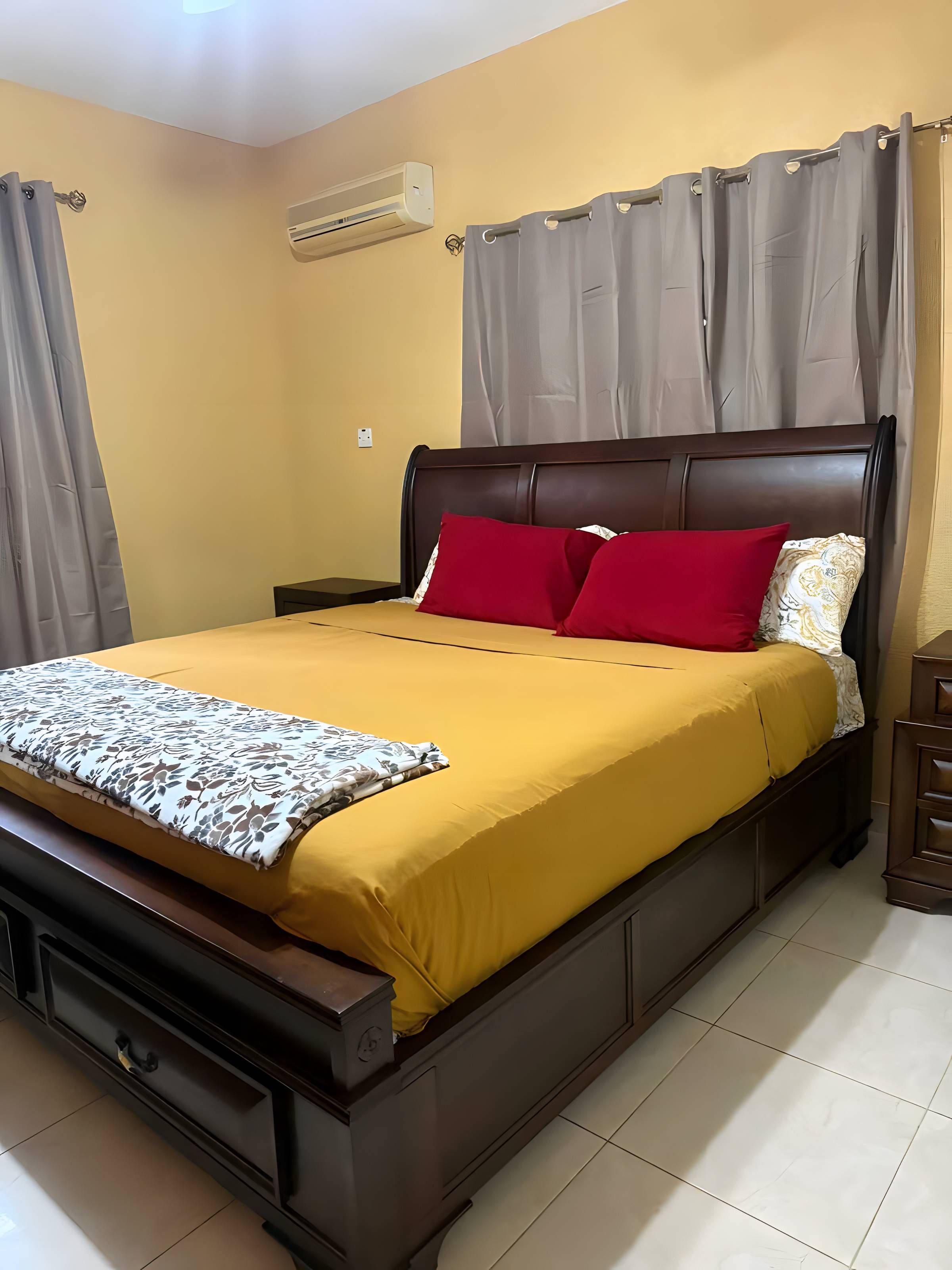 Uma cama com cabeceira, mesa de cabeceira e cortinas.