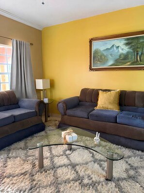 Ein Wohnzimmer mit zwei Sofas, einem Glastisch und einem Bild an der Wand.