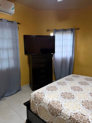 Ein Schlafzimmer mit einem Bett, einem Schminktisch, einem Fernseher und Vorhängen.