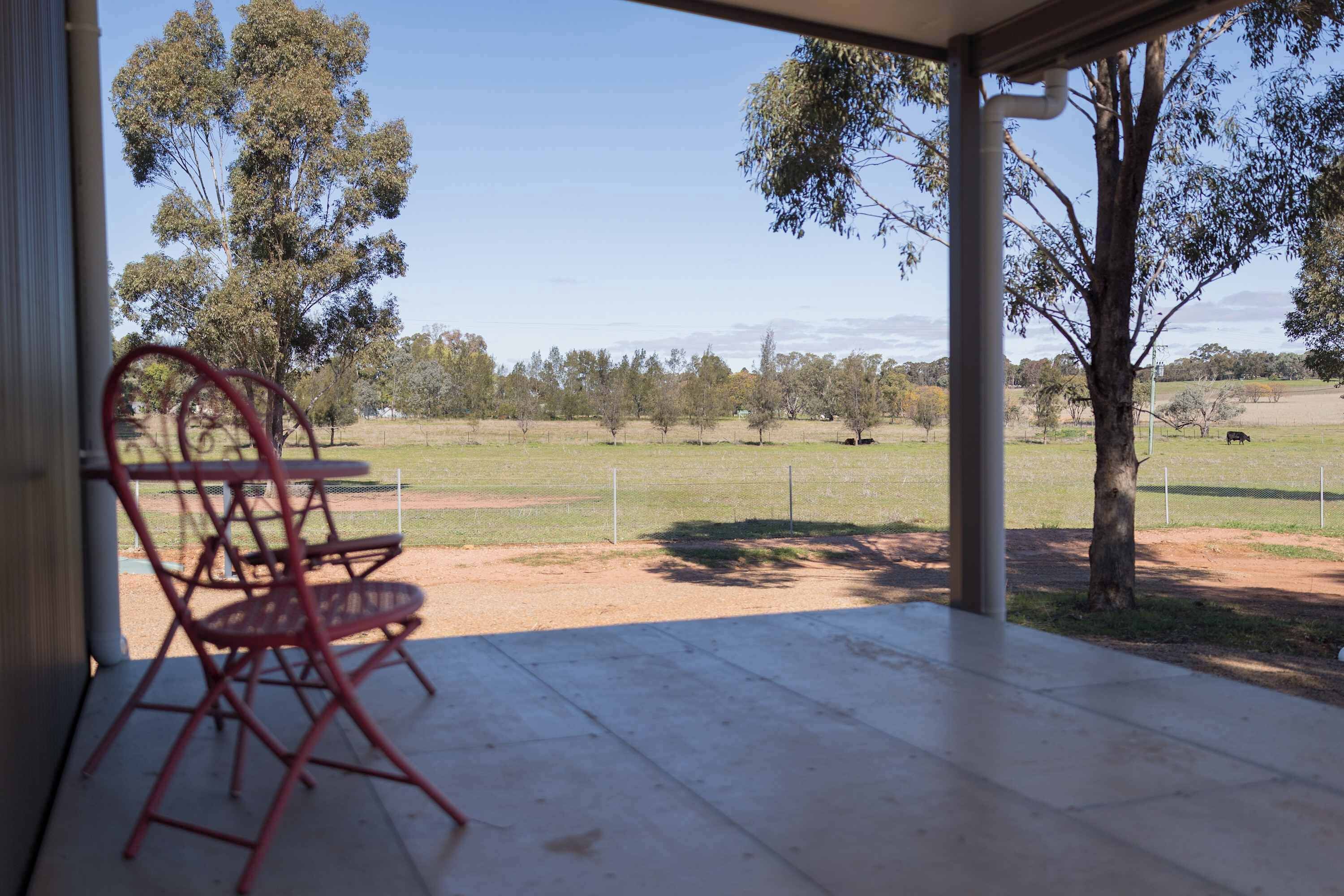 An outdoor patio with a table and chairs, overlooking a fenced field with trees and a distant view of hills.