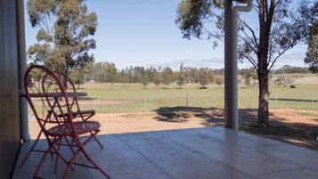 An outdoor patio with a table and chairs, overlooking a fenced field with trees and a distant view of hills.