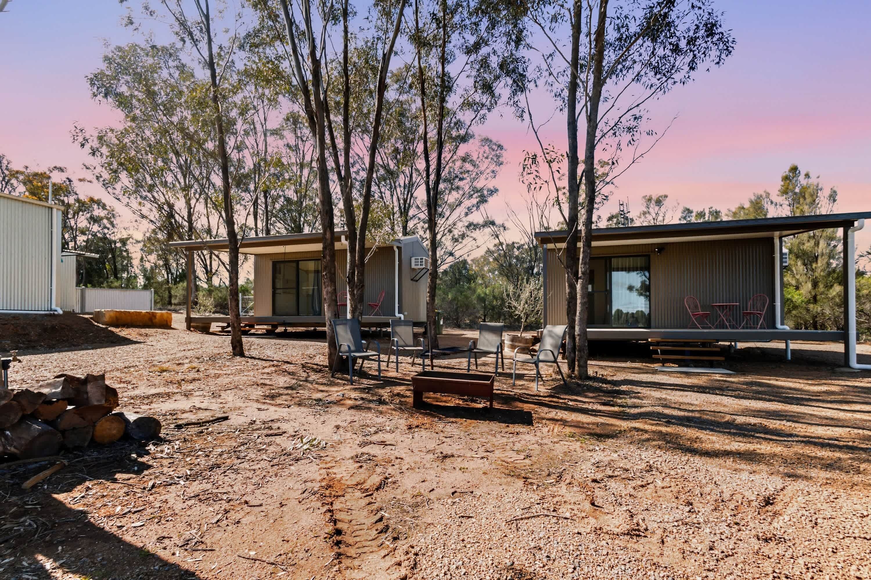 Un terrain de camping comprenant deux cabanes, un espace extérieur aménagé pour s’asseoir et une pile de bois de chauffage.